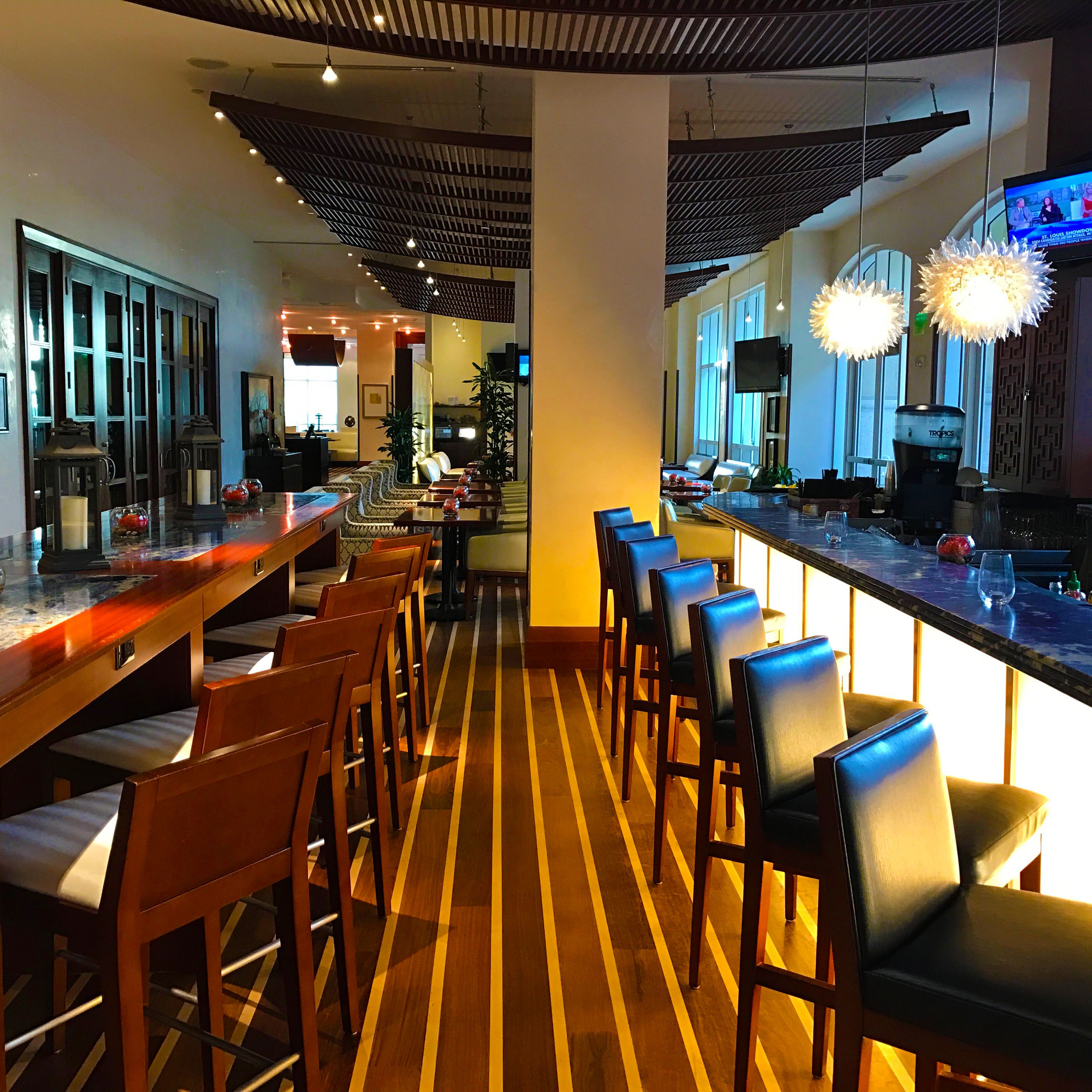 Uma área de bar moderna com piso de madeira, banquetas e um balcão comprido.