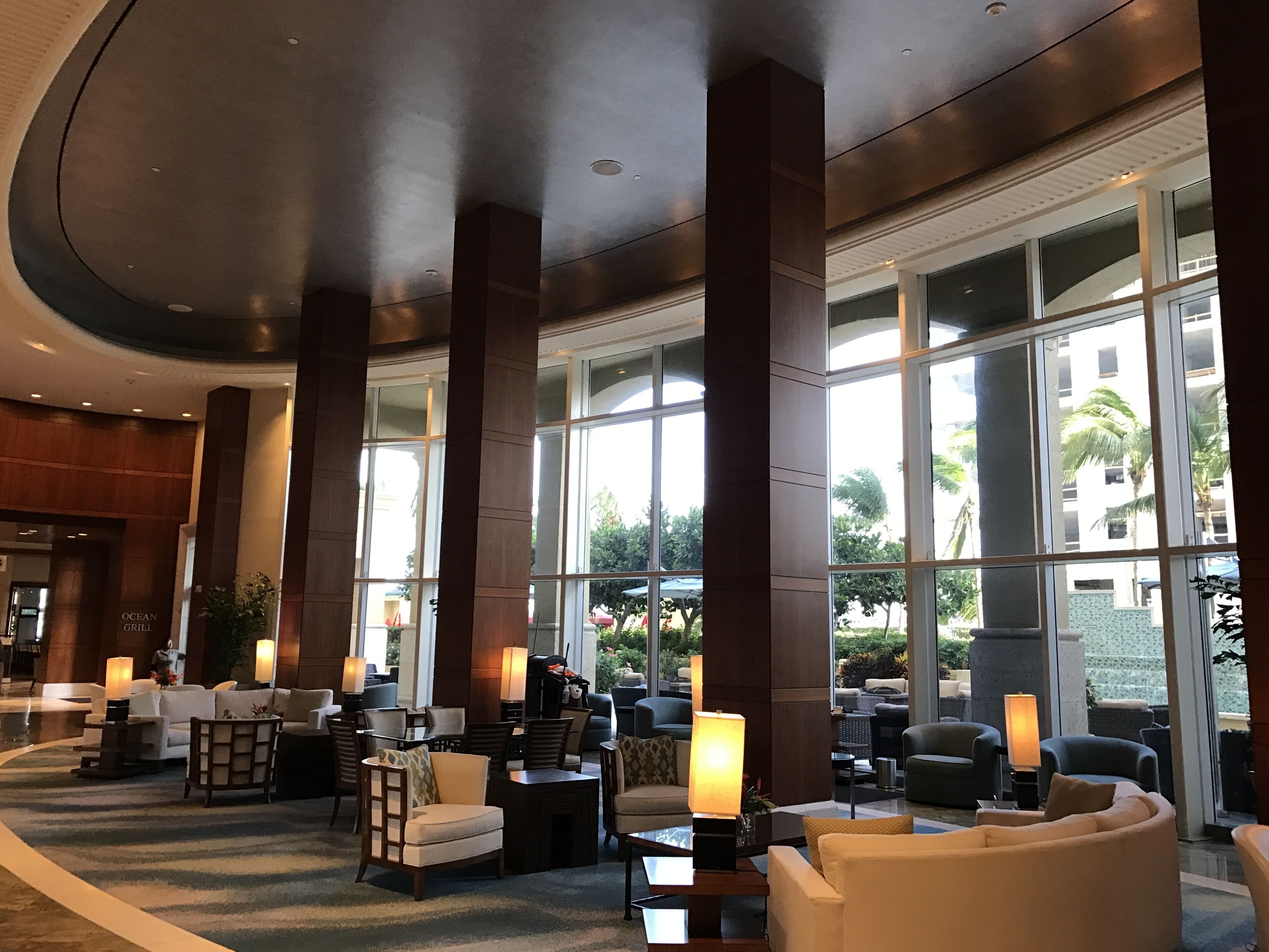 Eine Lobby mit hohen Decken, großen Fenstern und verschiedenen Sitzgelegenheiten, darunter Sofas und Sessel.