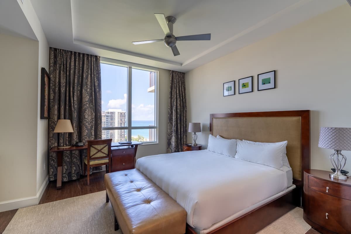 Habitación de hotel con una cama grande, un escritorio, una silla, un ventilador de techo y vistas a la ciudad.