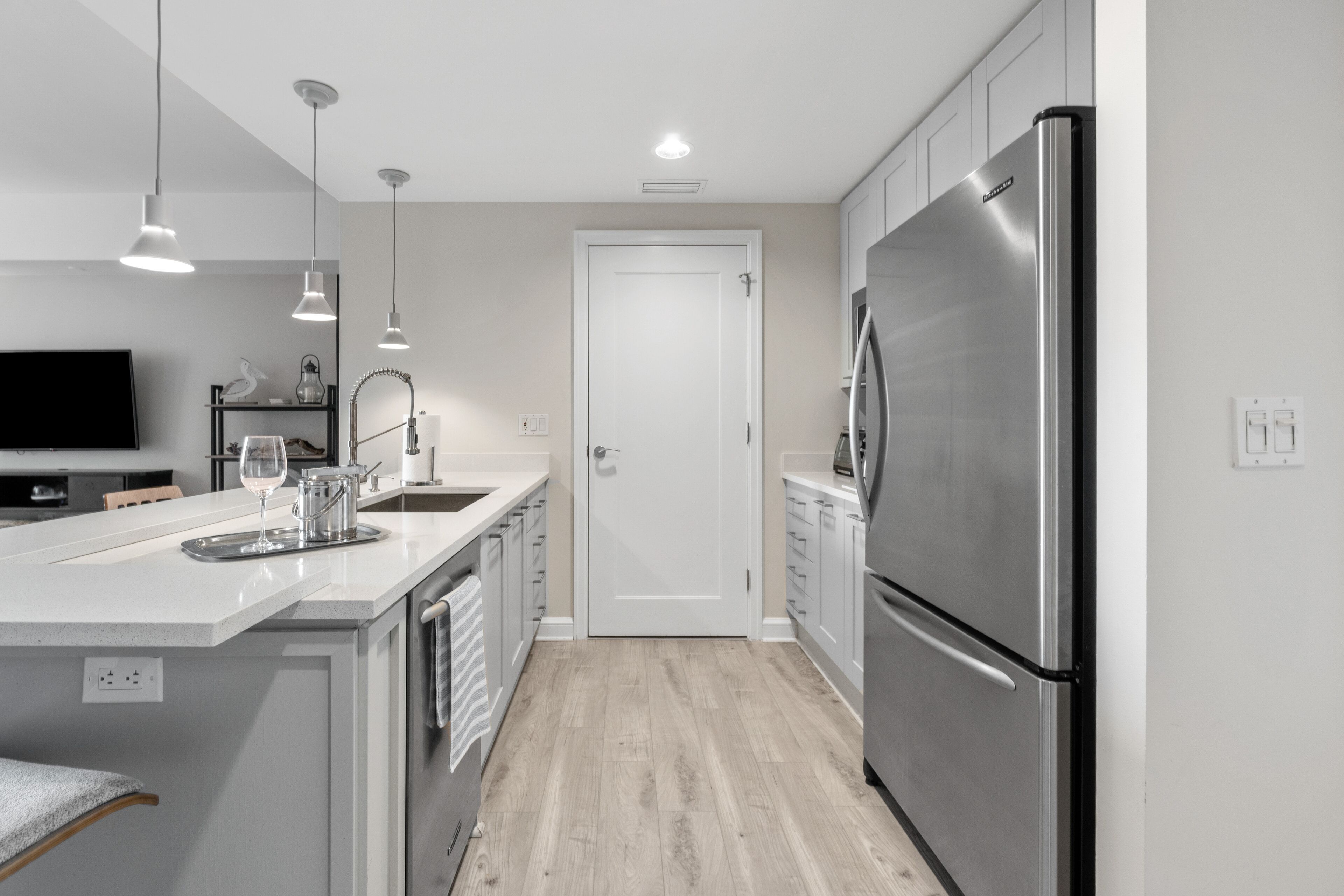 A modern kitchen with a stainless steel refrigerator, white cabinetry, and a central island with a sink and countertop.