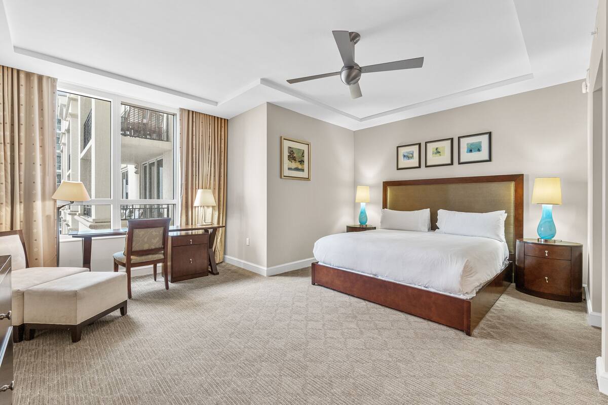 Una habitación de hotel con una cama grande, un escritorio, una silla y un ventilador de techo.