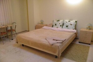 Un dormitorio ordenado con cama, mesitas de noche, una silla y una pequeña mesa.