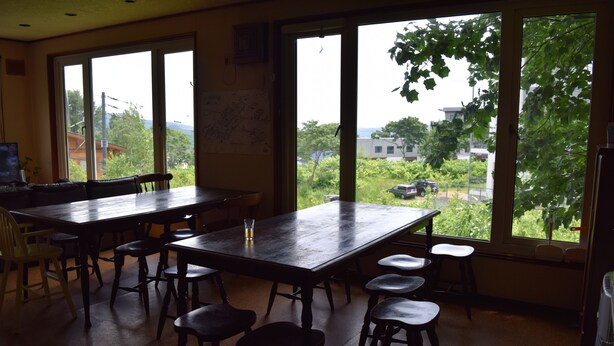 A dining area with a large table and multiple chairs, large windows with a view of greenery and buildings outside.
