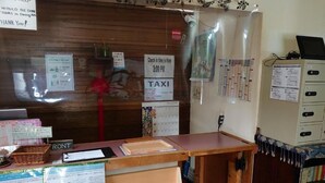 A reception desk with a sign indicating check-in time from 3:00 PM, a 'TAXI' sign, and various informational posters.