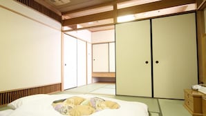 Een traditionele Japanse kamer met tatami vloeren, een laag houten bed, schuifdeuren en een klein houten dressoir.