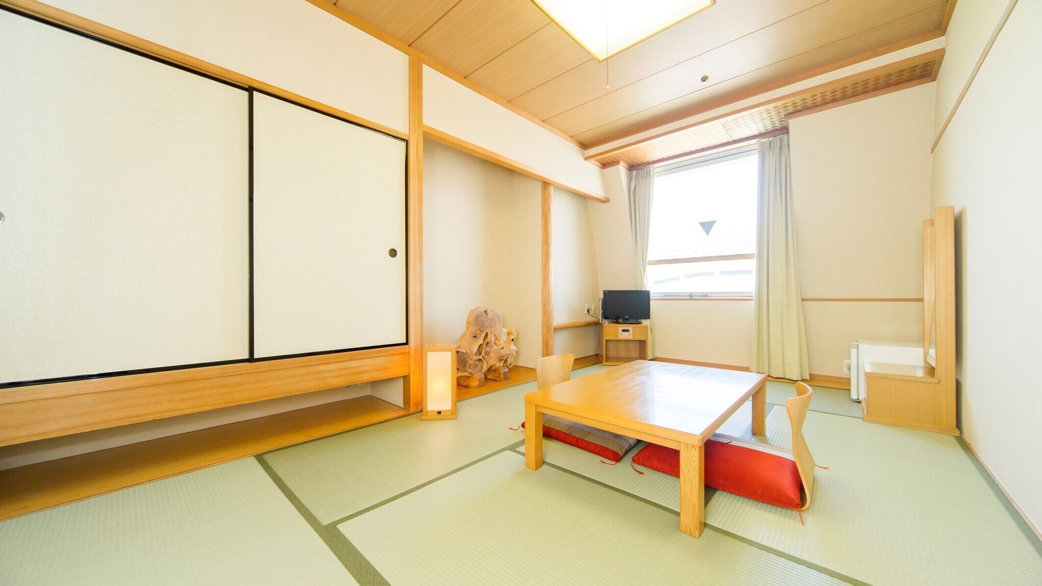 A traditional Japanese-style room with tatami flooring, a low wooden table, a television, and sliding doors.