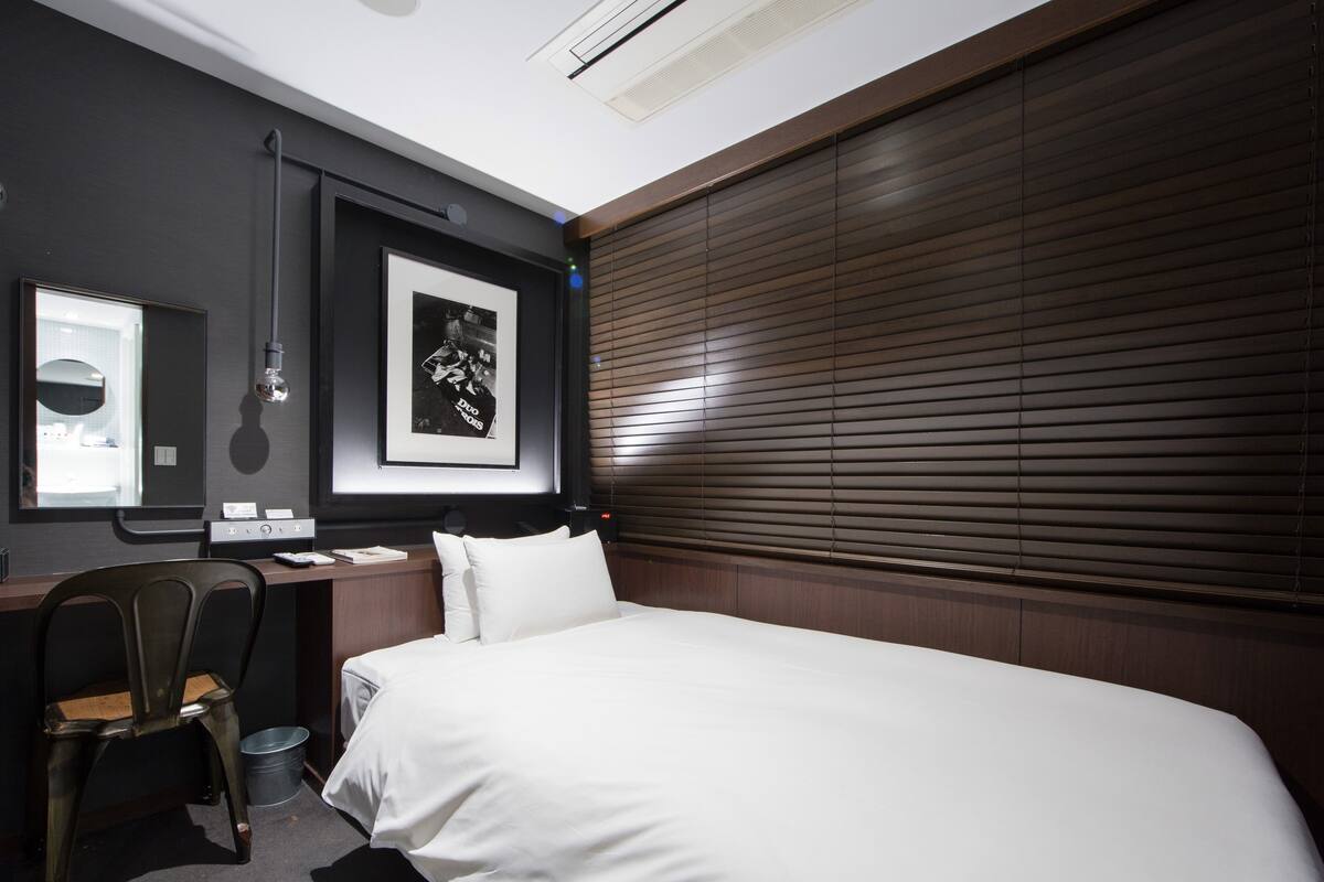 A hotel room with a large bed, a desk with a chair, a mirror, and a framed picture on the wall.