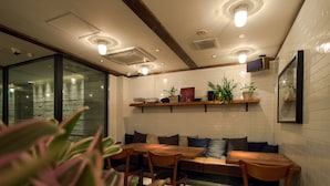 A modern dining area with wooden tables and chairs, a built-in bench, and potted plants on shelves. - Rock Star Hotel (Osaka)