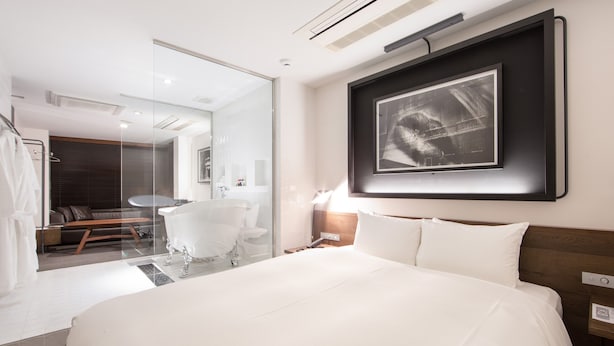 A modern hotel room with a large bed, a glass-enclosed bathroom, a mounted artwork, and a wooden headboard. - Rock Star Hotel (Osaka)