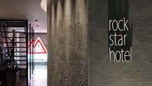 A hallway with a sign for the Rock Star Hotel, a caution sign, and a plant. - Rock Star Hotel (Osaka)