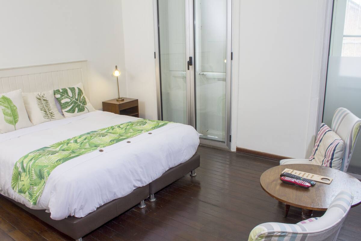 A hotel room with a bed, a nightstand, a chair, and a table with a remote control.
