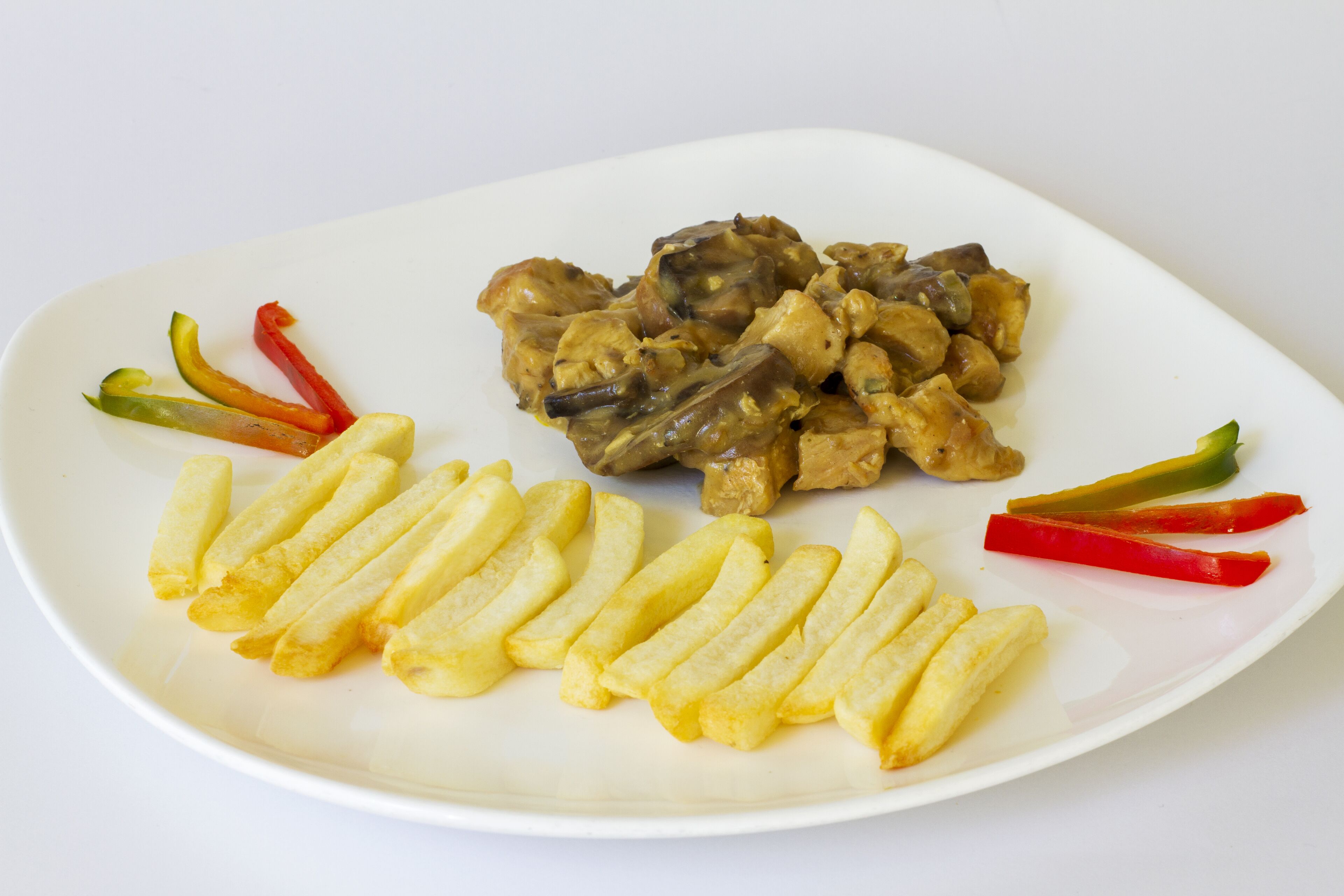 Un plato blanco con un guiso de pollo y champiñones, papas fritas y pimiento en rodajas.