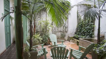 A courtyard with green chairs and tables, surrounded by potted plants and palm trees.