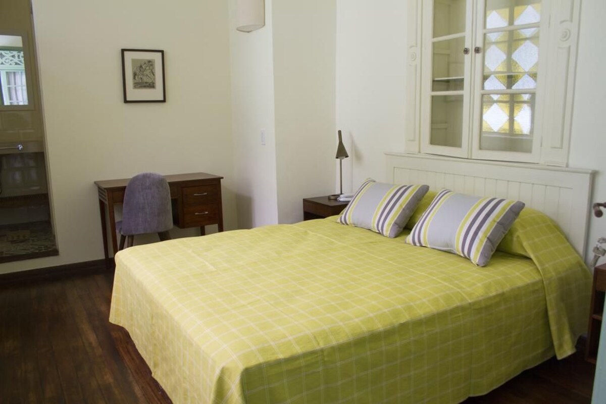 A bedroom with a bed, a desk, a chair, a lamp, and a cabinet with glass doors.