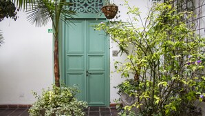 A green door with a decorative panel, a hanging basket, and various potted plants. - Hotel Casa De La Vega (Bogotá)
