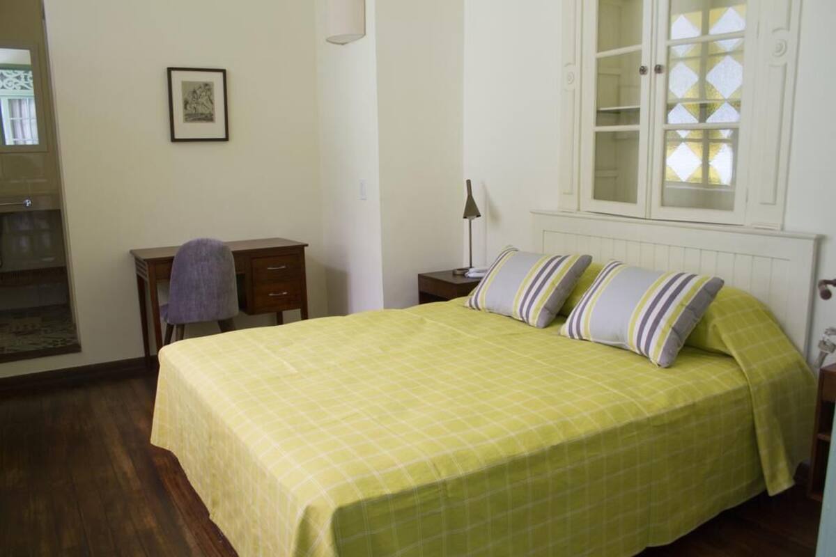 A bedroom with a bed, a desk, a chair, a lamp, and a cabinet with glass doors.