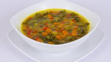 Un tazón blanco de sopa de verduras sobre un plato blanco.
