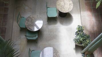 Vue aérienne d’une cour intérieure avec plusieurs tables et chaises rondes, entourée de plantes en pot et de verdure.