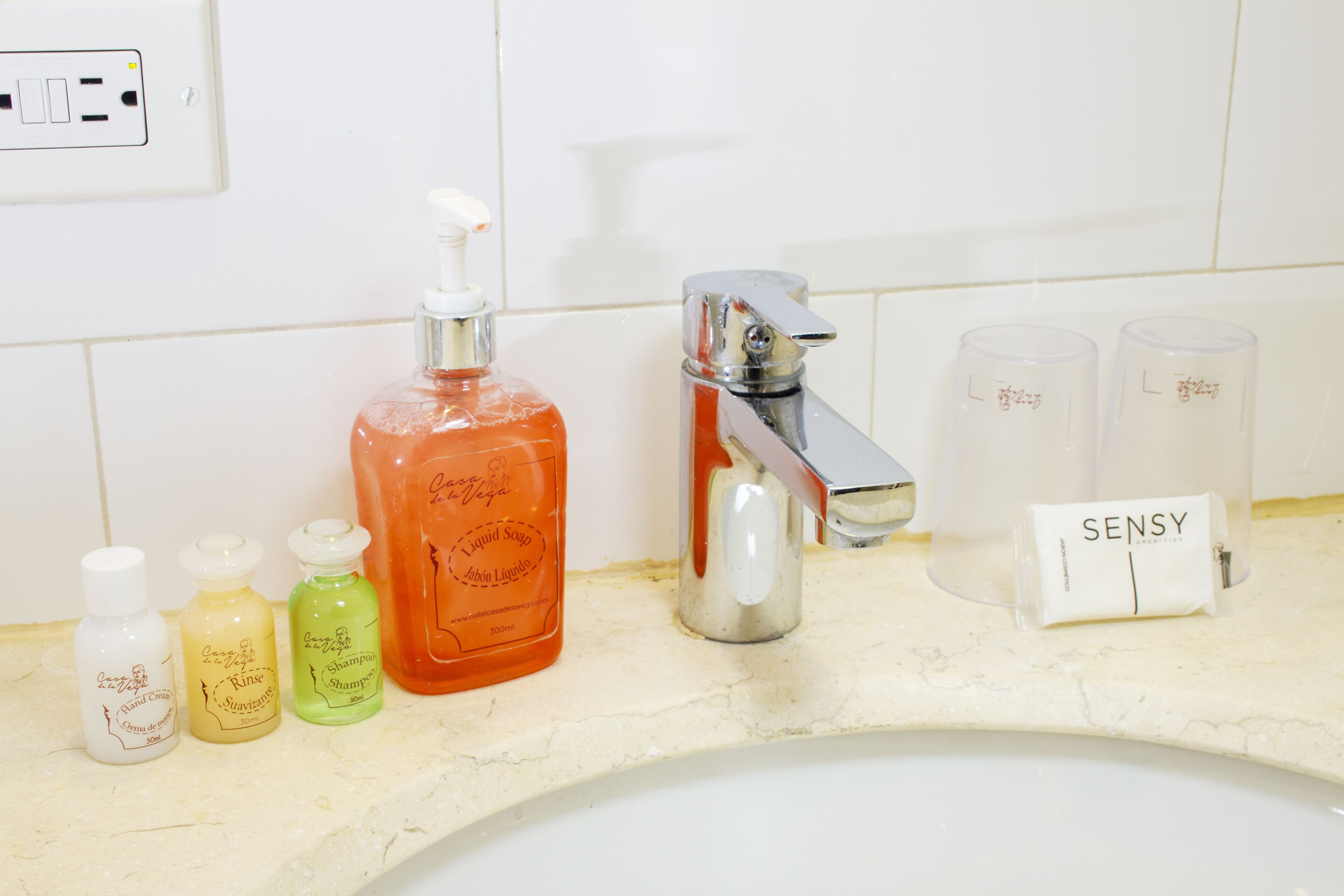Een wastafel in een badkamer met diverse toiletartikelen, zoals een fles vloeibare zeep, shampoo en handcrème.