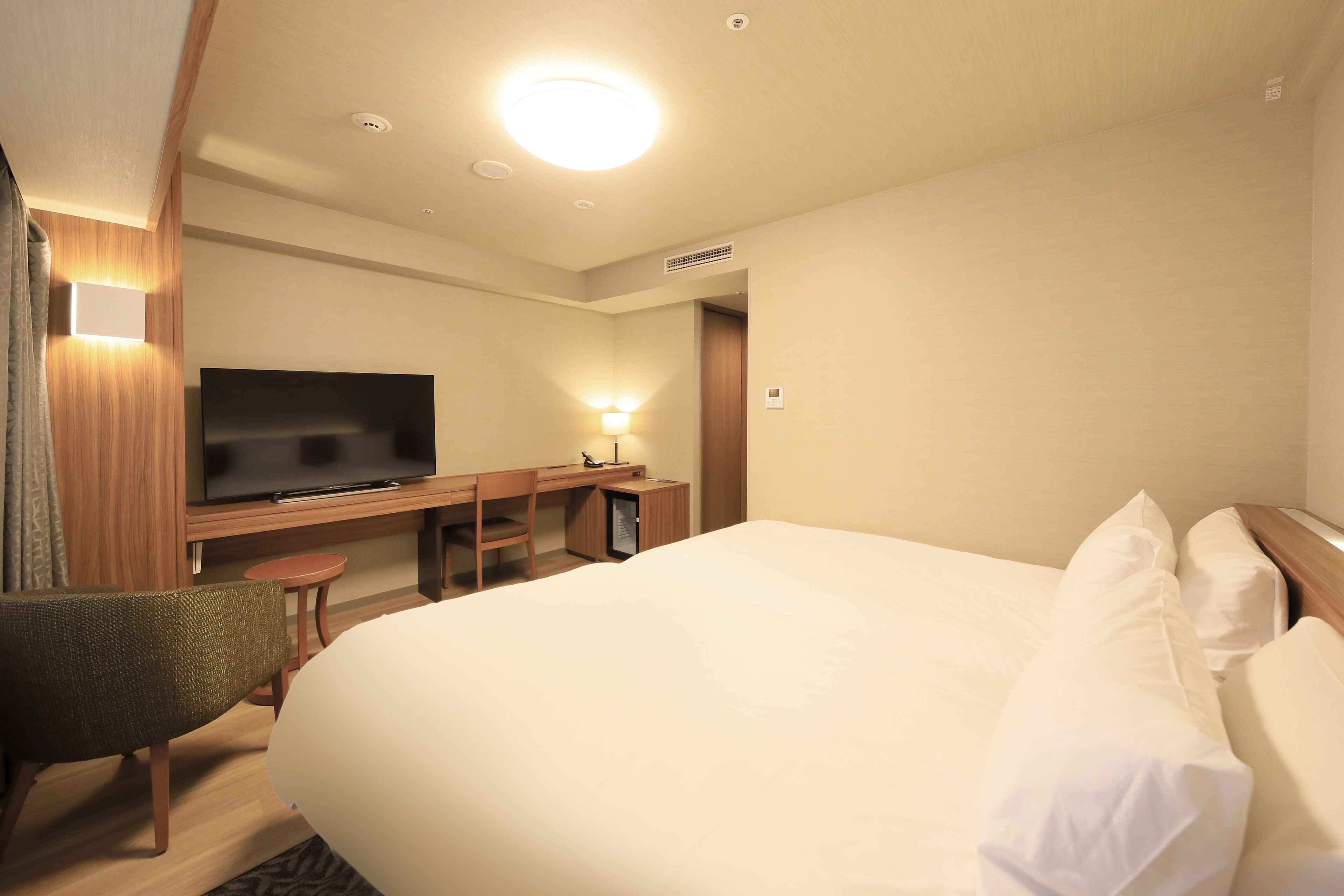 A hotel room with a large bed, a desk with a flat-screen TV, a chair, and a small table.