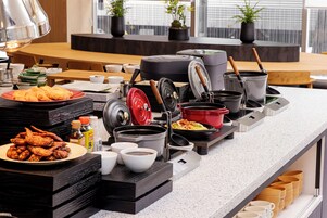A buffet setup with various dishes, cooking equipment, and dining ware.