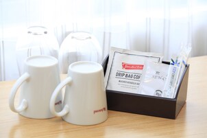 Dos tazas blancas de café, un sobre de café de filtro y una caja de leche condensada sobre una mesa de madera.