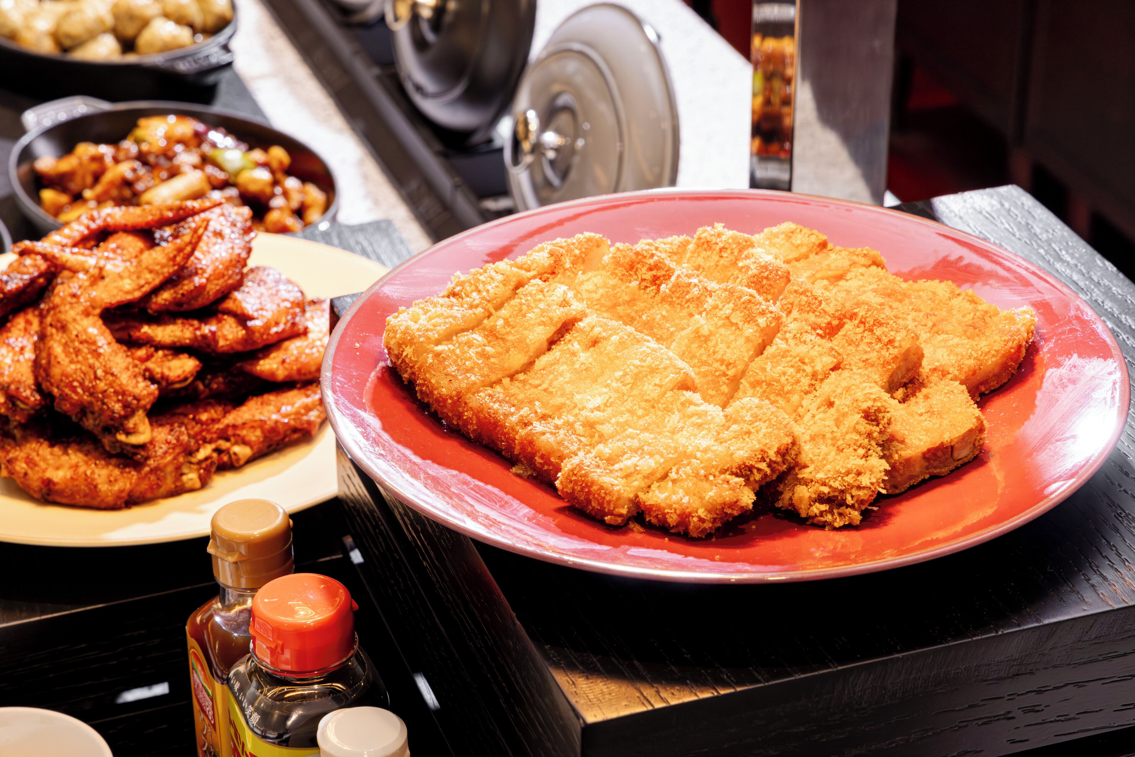 Uma mesa de jantar com diversos pratos, incluindo frango frito e um prato vermelho com escalopes empanados.