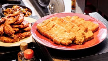 Uma mesa de jantar com diversos pratos, incluindo frango frito e um prato vermelho com escalopes empanados.