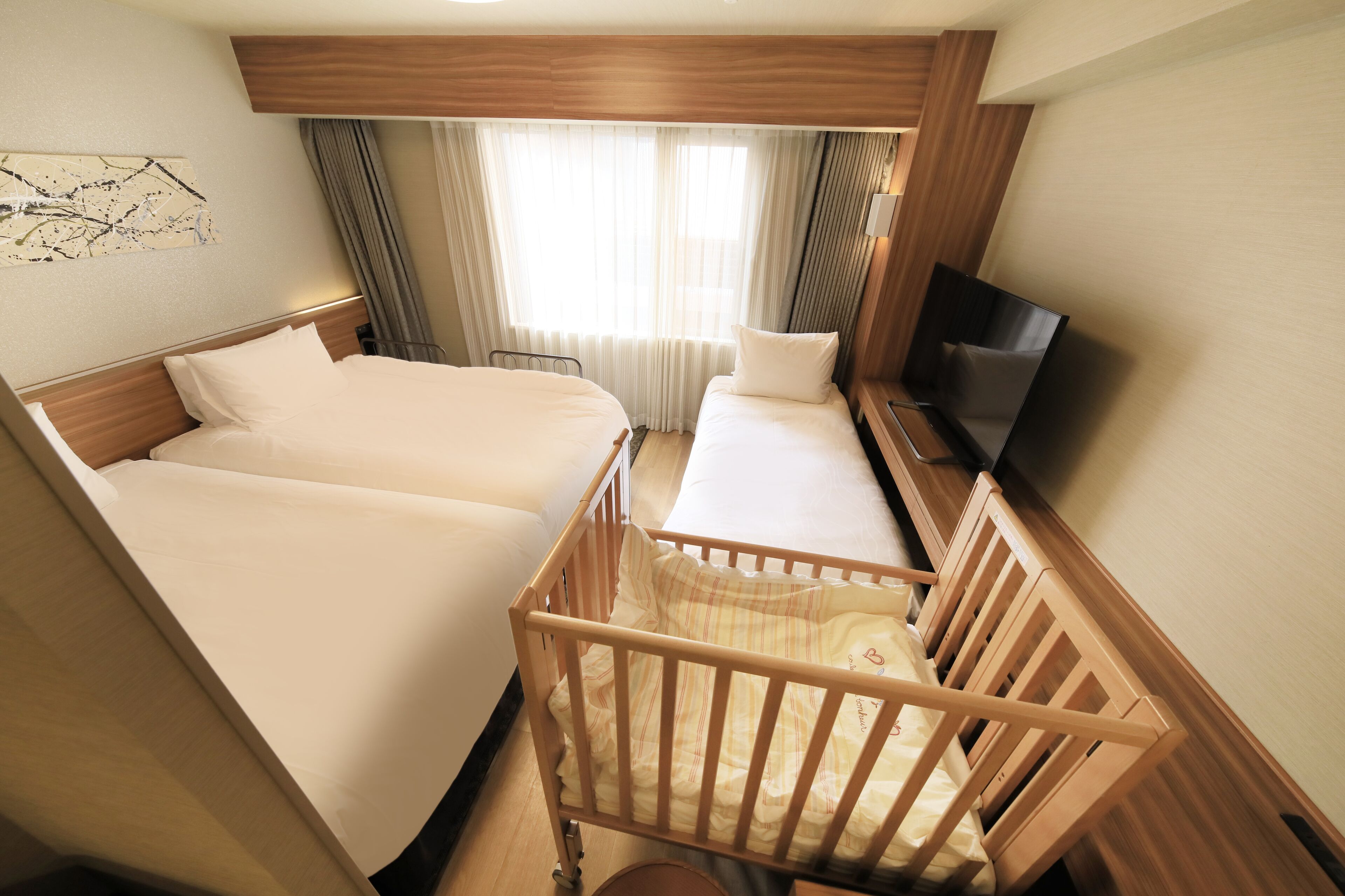 Una habitación de hotel con dos camas, televisión y una cuna.