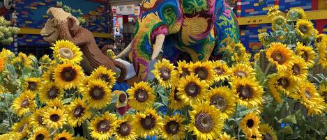 A colorful LEGO sculpture of an elephant surrounded by sunflowers.
