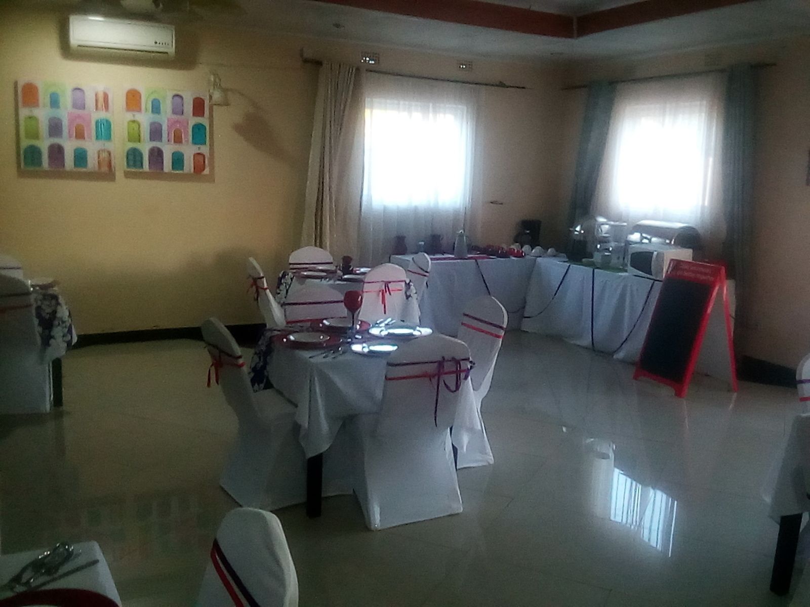 Un espace repas avec des tables dressées pour le repas, des chaises ornées de rubans rouges et un panneau indicateur rouge.