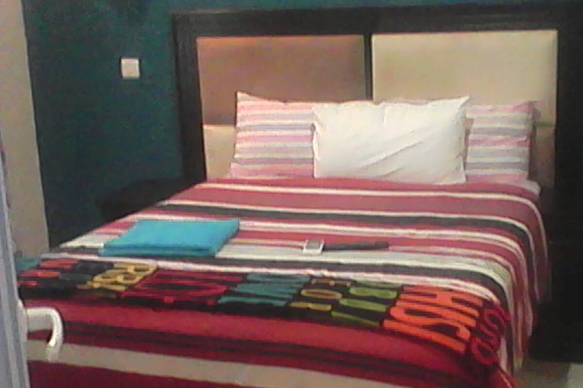 Una cama con una colcha a rayas, una almohada y un libro azul encima.