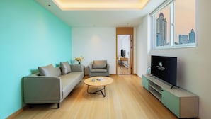Una sala de estar moderna con sofá, sillón, mesa de centro, televisor y vista a la ciudad a través de un ventanal grande.