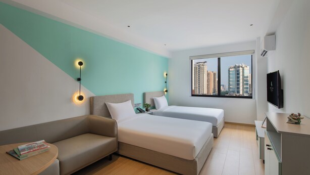 Una habitación de hotel moderna con sofá, dos camas, una mesita y un televisor.