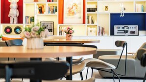 Una sala de estar moderna con una mesa redonda, sillas, un sofá y una estantería llena de libros y objetos decorativos.