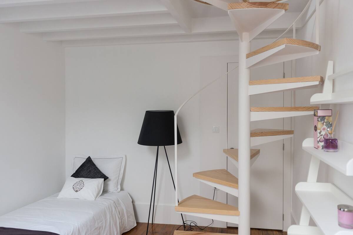 Une chambre à coucher avec un lit, un lampadaire noir, un mur blanc et un escalier en colimaçon blanc.