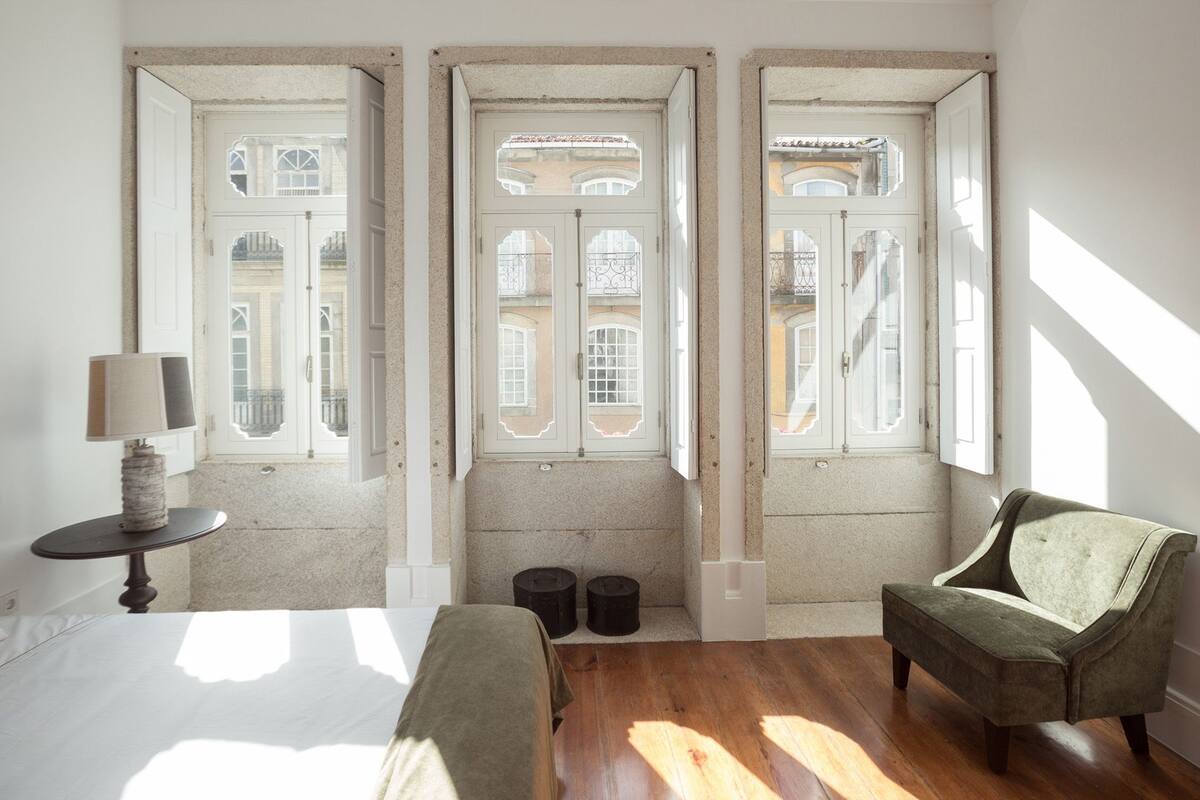 Une pièce avec trois fenêtres, un lit, une chaise et une lampe.