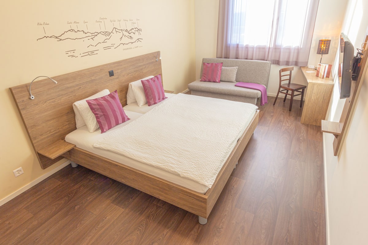 Quarto com uma cama grande, um sofá, uma escrivaninha e uma cadeira.