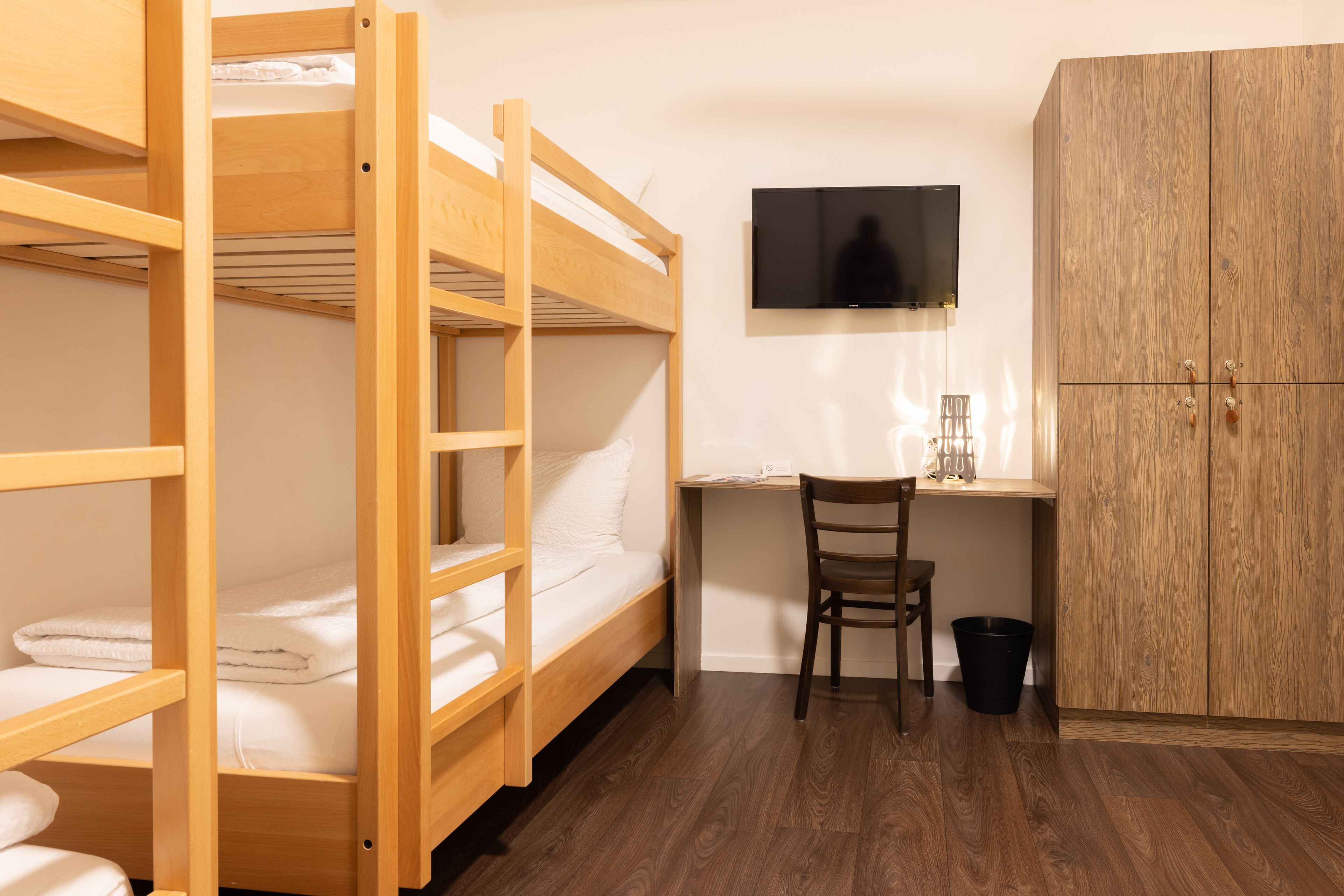 A bunk bed room with a desk and chair, a television, and a wardrobe.