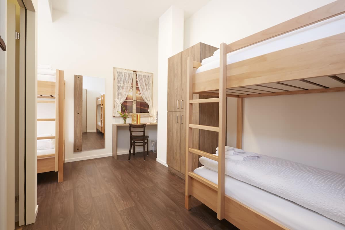 Um quarto com uma cama beliche, uma escrivaninha com cadeira e um espelho.