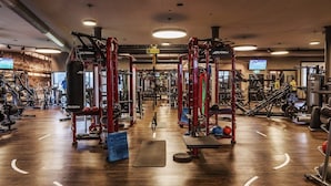 Un gimnasio con diversos equipos de ejercicio, suelo de madera y una pantalla de televisión en la pared.