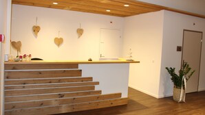 Un mostrador de recepción con detalles de madera, una pared blanca con una puerta que dice “Privado” y una planta en maceta a la derecha.