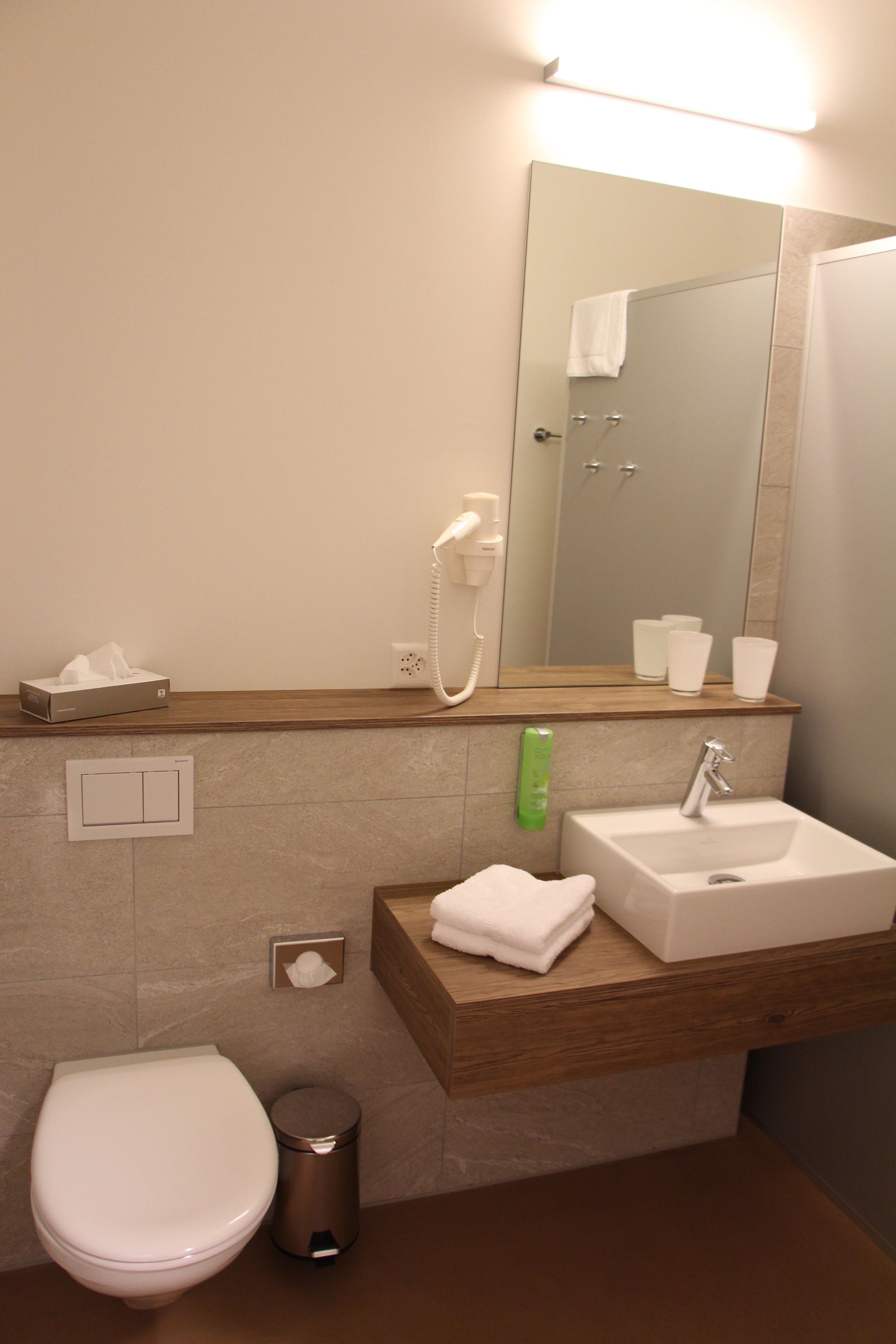 Un baño moderno con inodoro, lavamanos y espejo sobre el lavamanos.