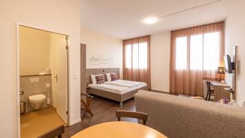 Habitación de hotel con cama, escritorio, silla, mesa, televisión y baño.