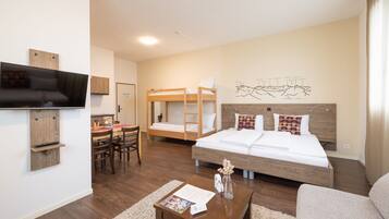 A modern hotel room with a large bed, a TV mounted on the wall, a desk with a chair, and a bunk bed.