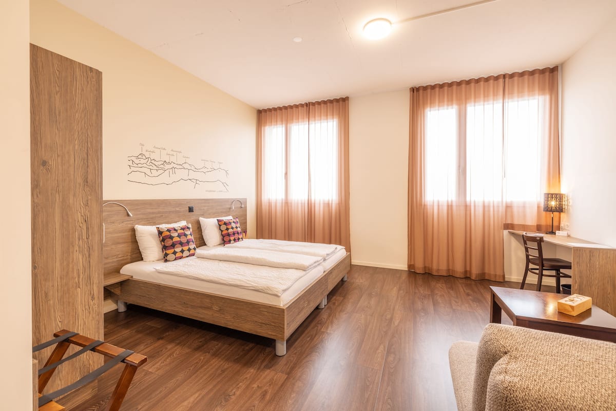 Quarto com cama de madeira, uma escrivaninha e uma cadeira.