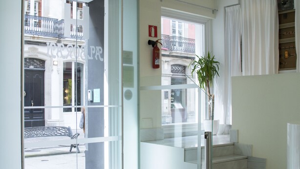 Un moderno vestíbulo de hotel con un puerta de vidrio que da a la calle, una escalera y un área de descanso con una mesa y sillas.