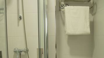A bathroom with a glass-enclosed shower, a toilet, and a towel rack with a folded towel.