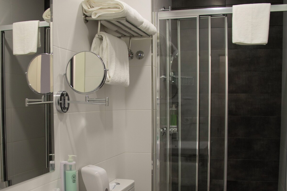 Un baño moderno con un lavamanos blanco, un inodoro, una cabina de ducha de vidrio y un espejo.