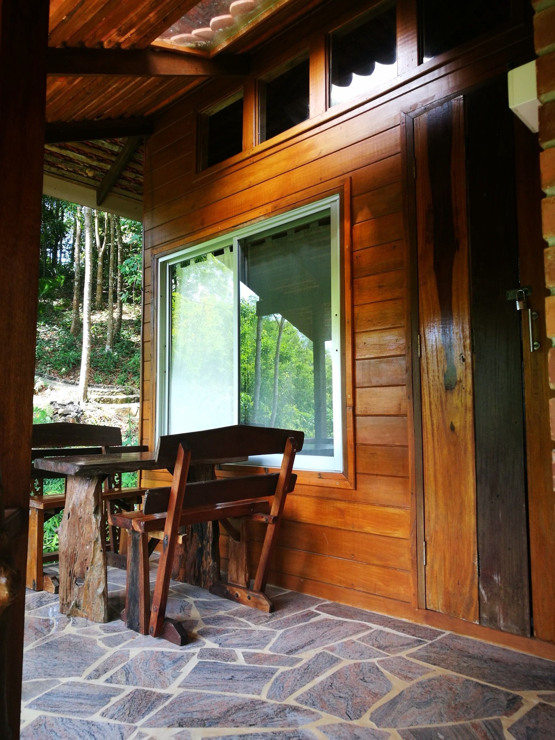 A wooden cabin with a stone-tiled porch, a wooden bench, and a table.